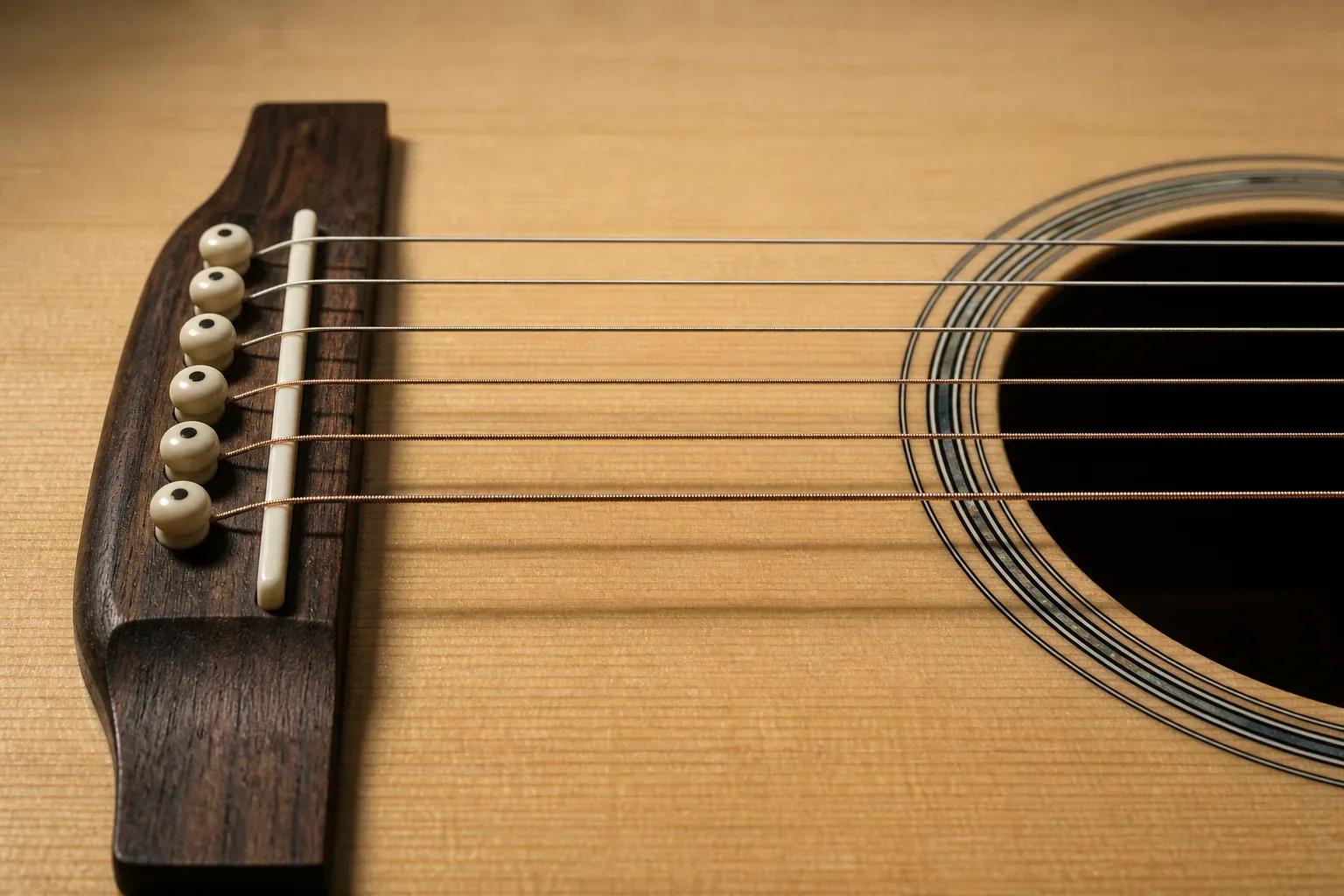 Macro view of six acoustic guitar strings crossing a wooden bridge and saddle toward the soundhole in warm raking light
