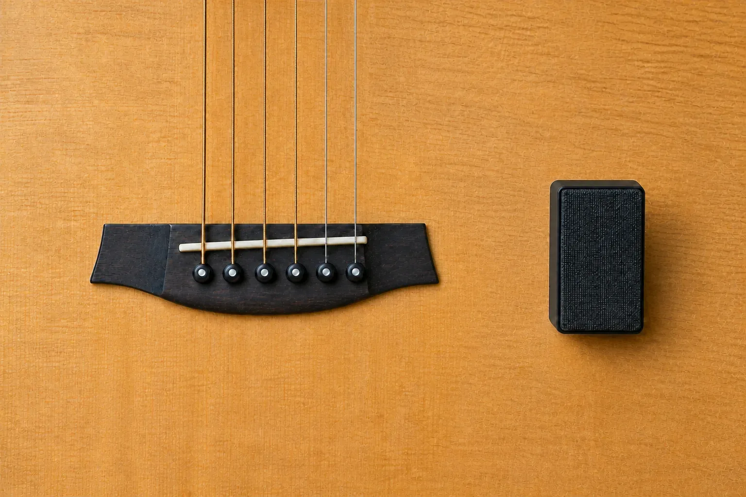 Six-string acoustic guitar bridge beside a small blank recording monitor on a warm wood soundboard