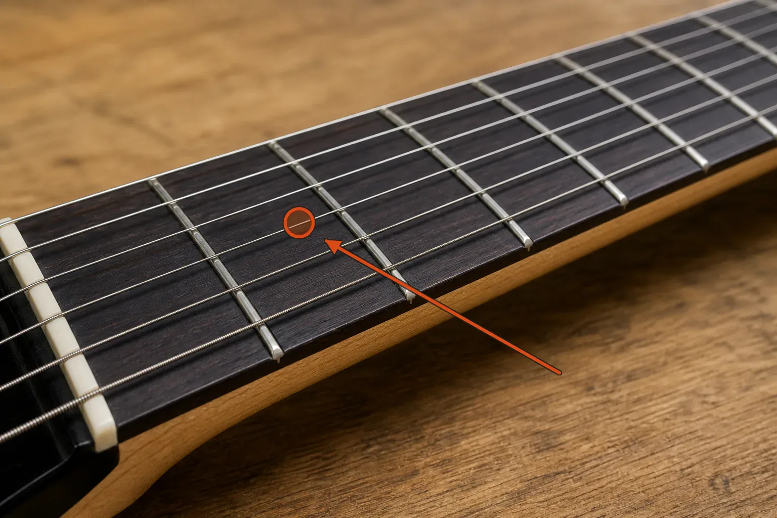 Close oblique view of a six-string guitar fretboard with an orange marker showing the narrow space immediately behind a fret