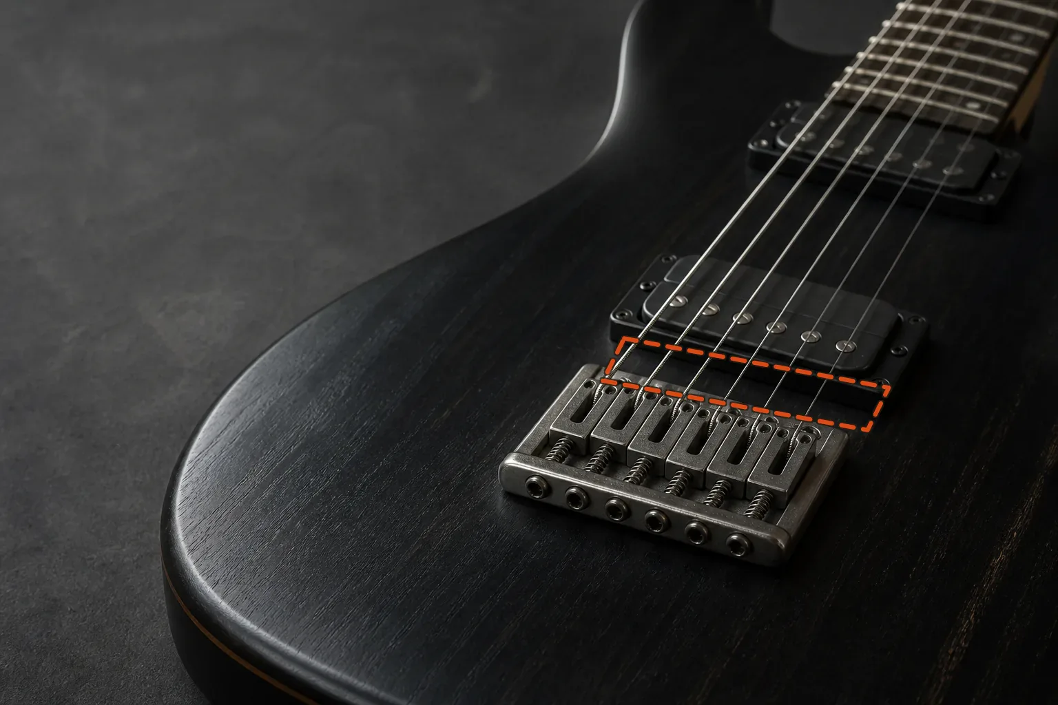 Six-string electric guitar bridge with an orange dashed zone across the strings between the saddles and bridge pickup