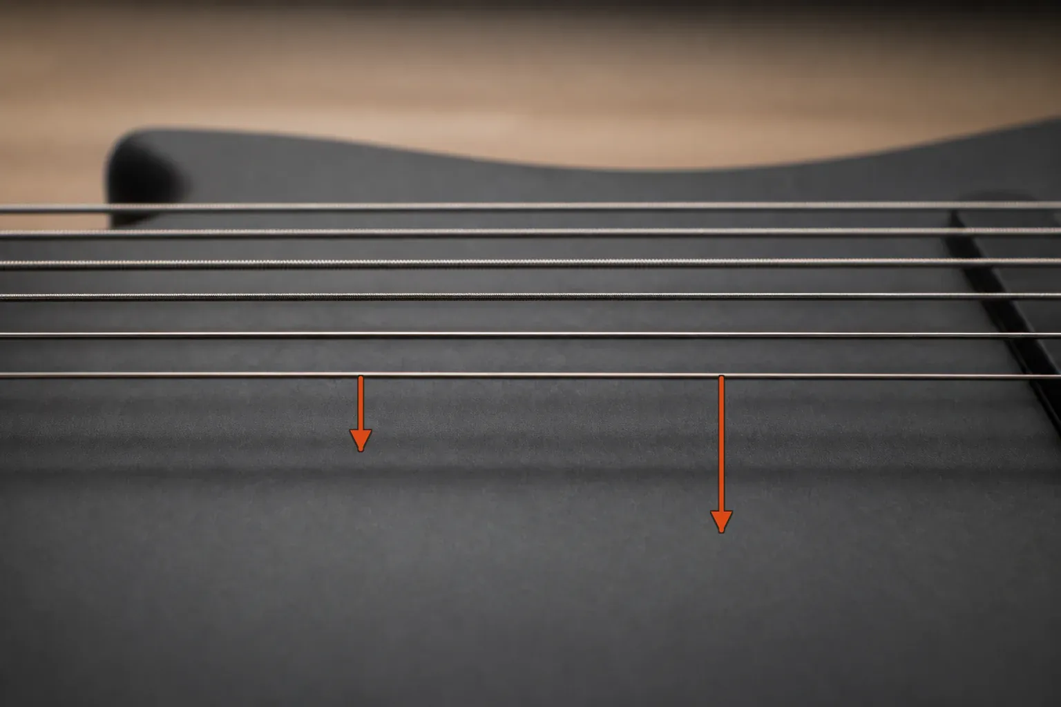 Low-angle view of six guitar strings above a dark guitar body with two orange depth gauges